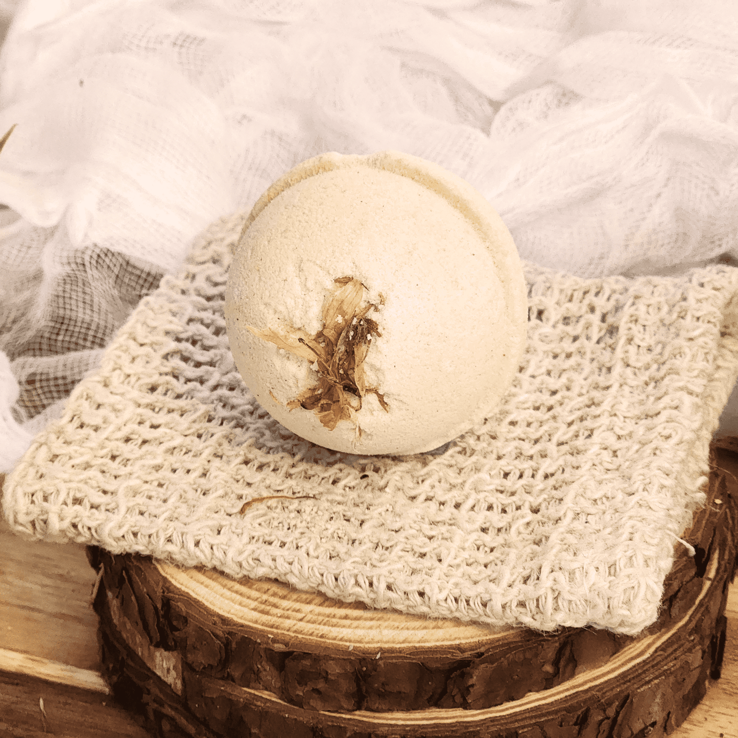 JOSSPURE grapefruit mini bath bomb resting on a textured beige cloth over a wooden surface
