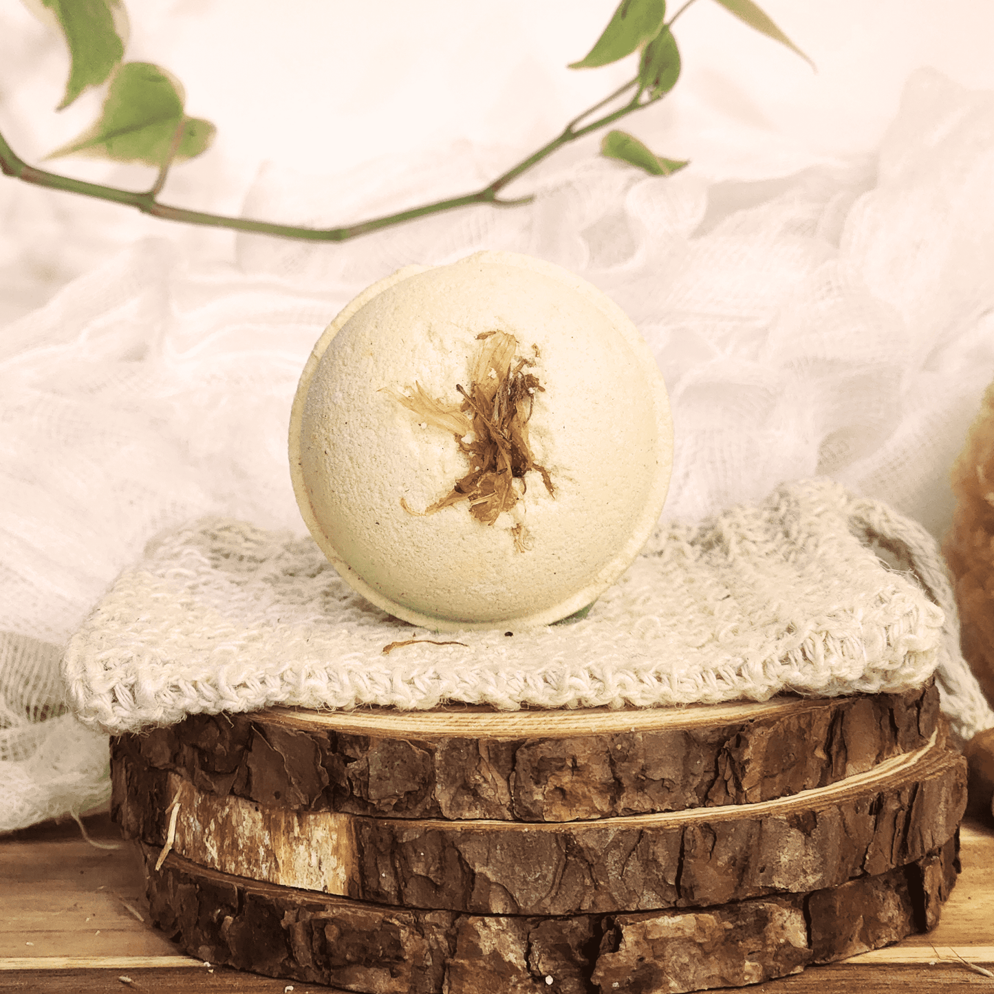 JOSSPURE grapefruit mini bath bomb with dried flower on top displayed on knitted cloth and wood slices