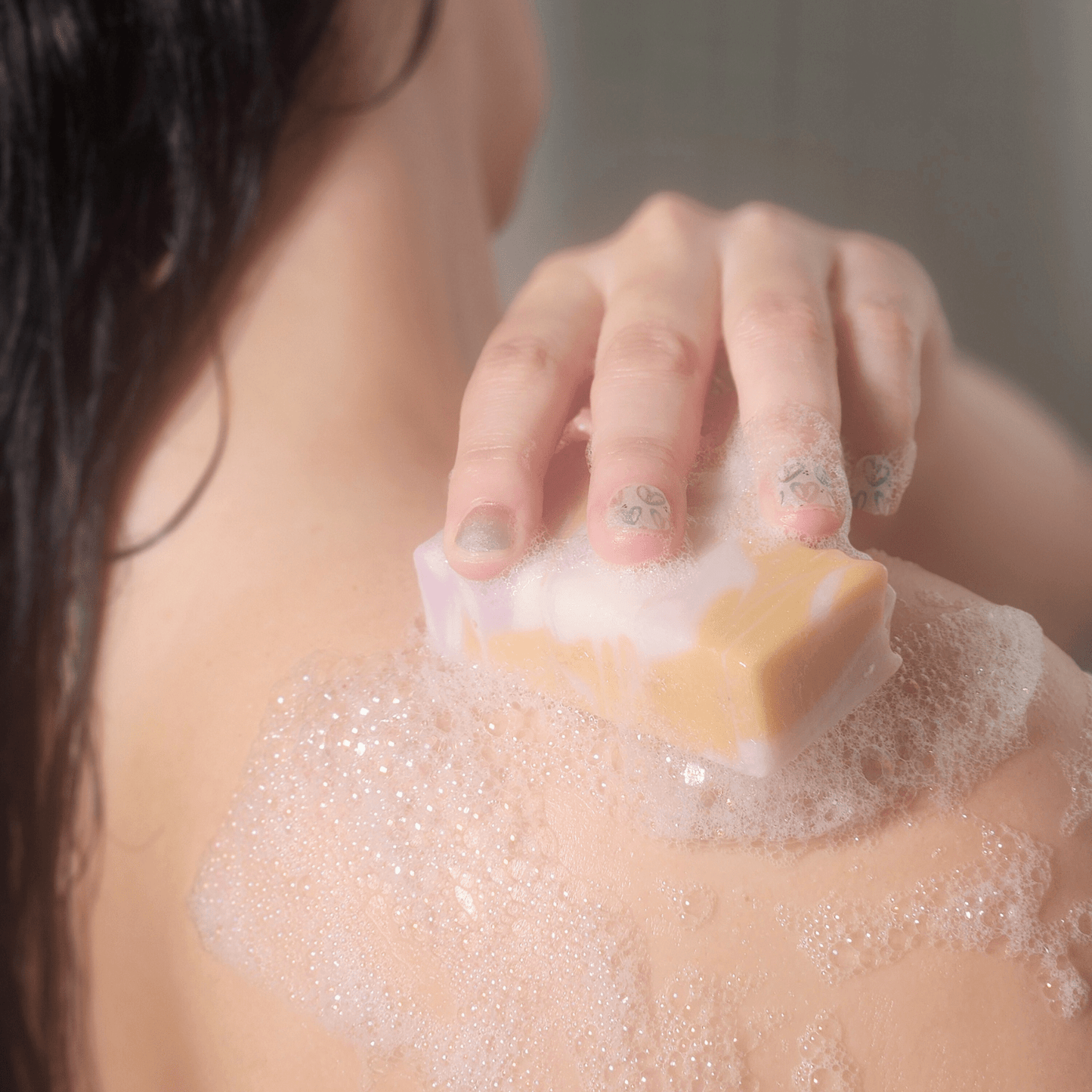 Person using Green All Natural Soap bar to create lather on shoulder during shower