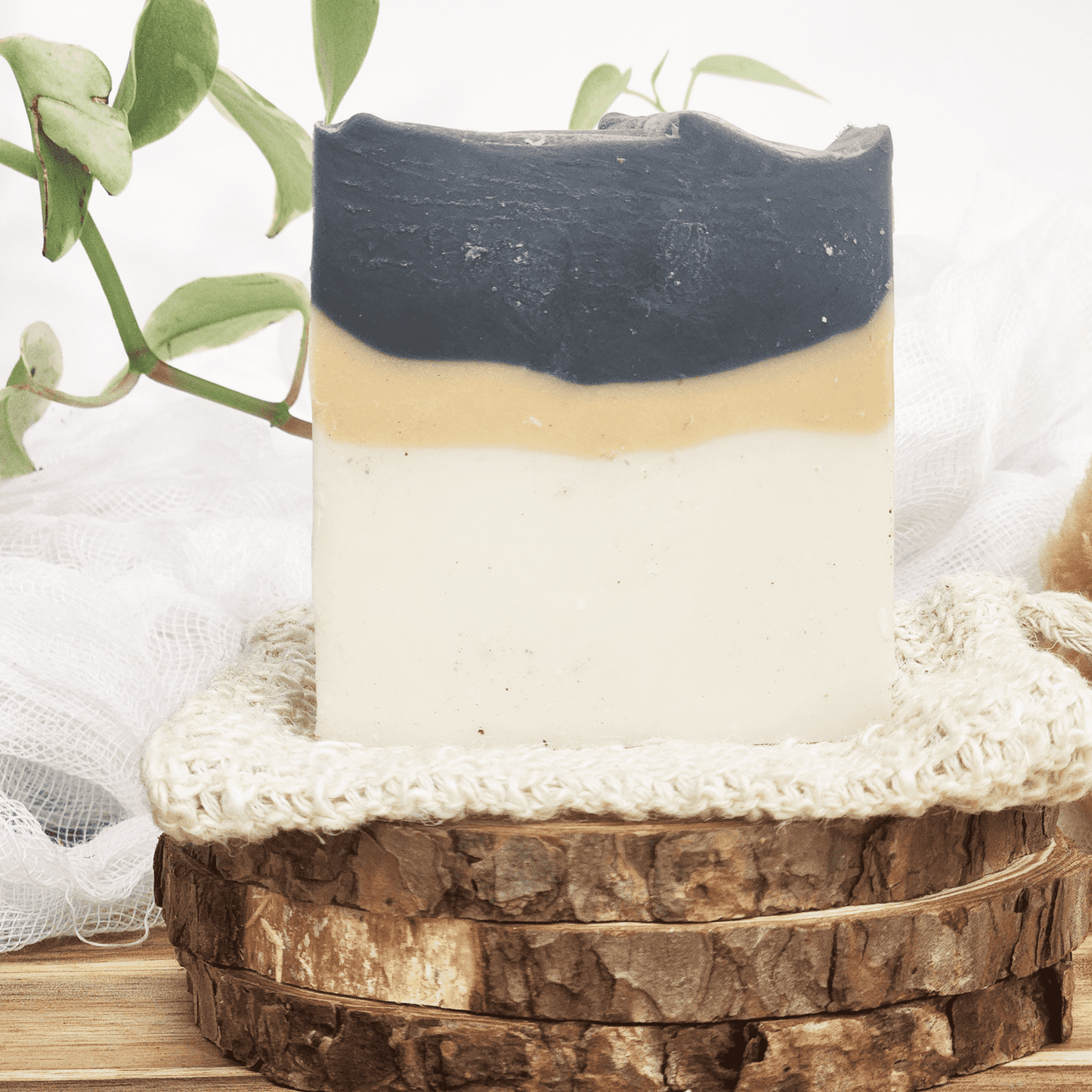 JOSSPURE charcoal unisex soap with black, beige, and white layers on a natural wooden soap dish