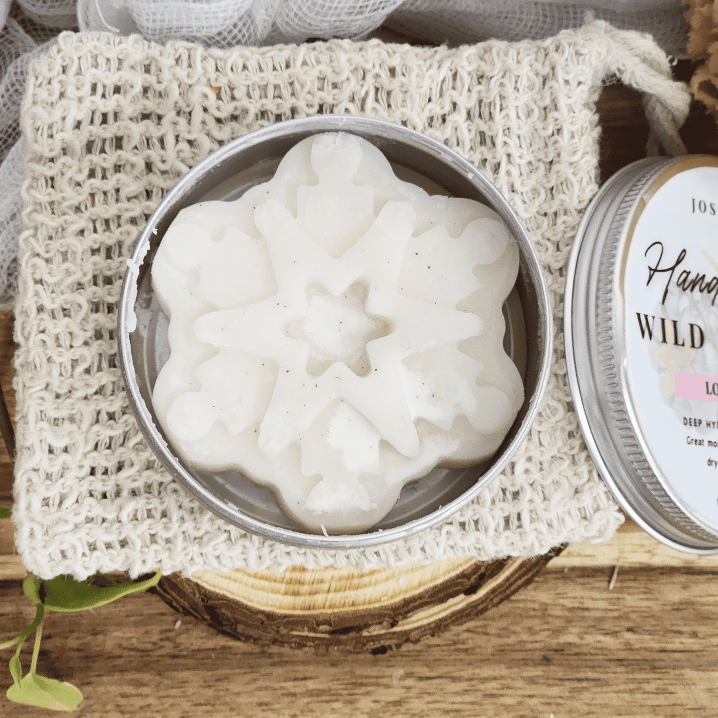 JOSSPURE handmade lotion bars shaped like a white snowflake in a metal tin on a textured cloth