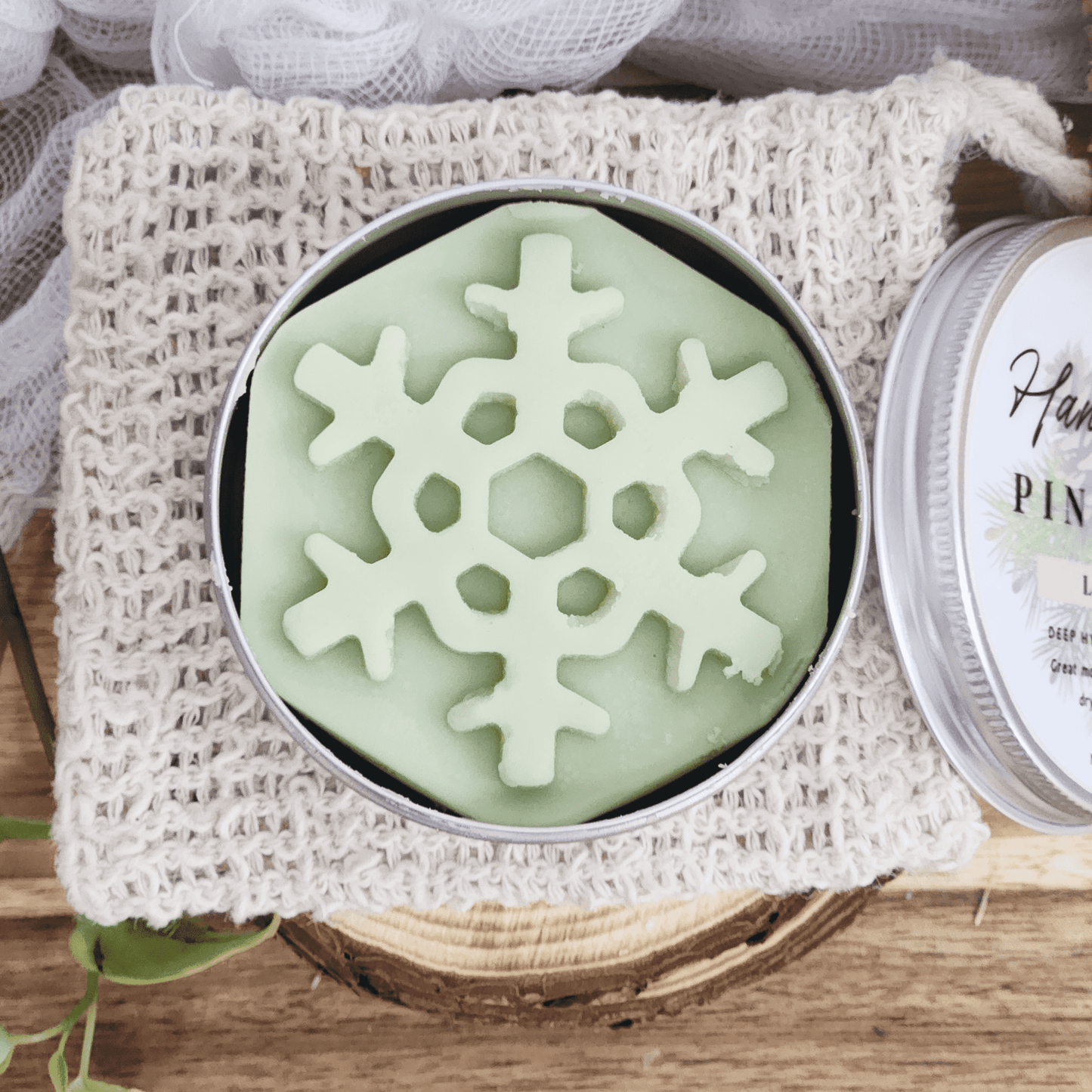 JOSSPURE handmade lotion bars shaped like a green snowflake in a round tin on a knitted pouch