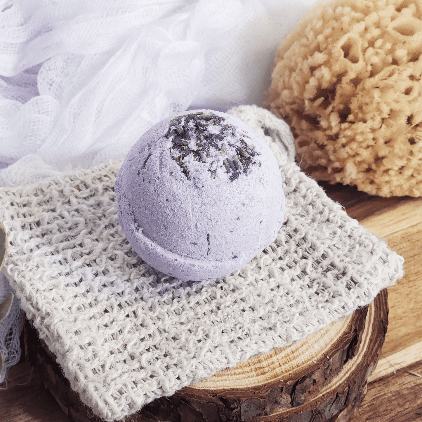 Lavender bath bomb with dried lavender on top placed on a natural woven cloth and wooden surface