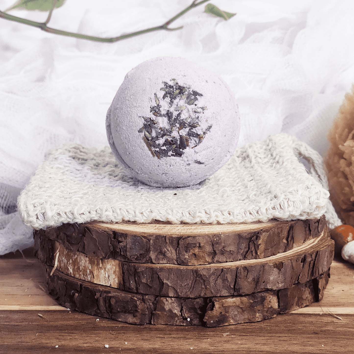 JOSSPURE lavender bath bomb with dried lavender on top placed on a knitted cloth over wooden slices