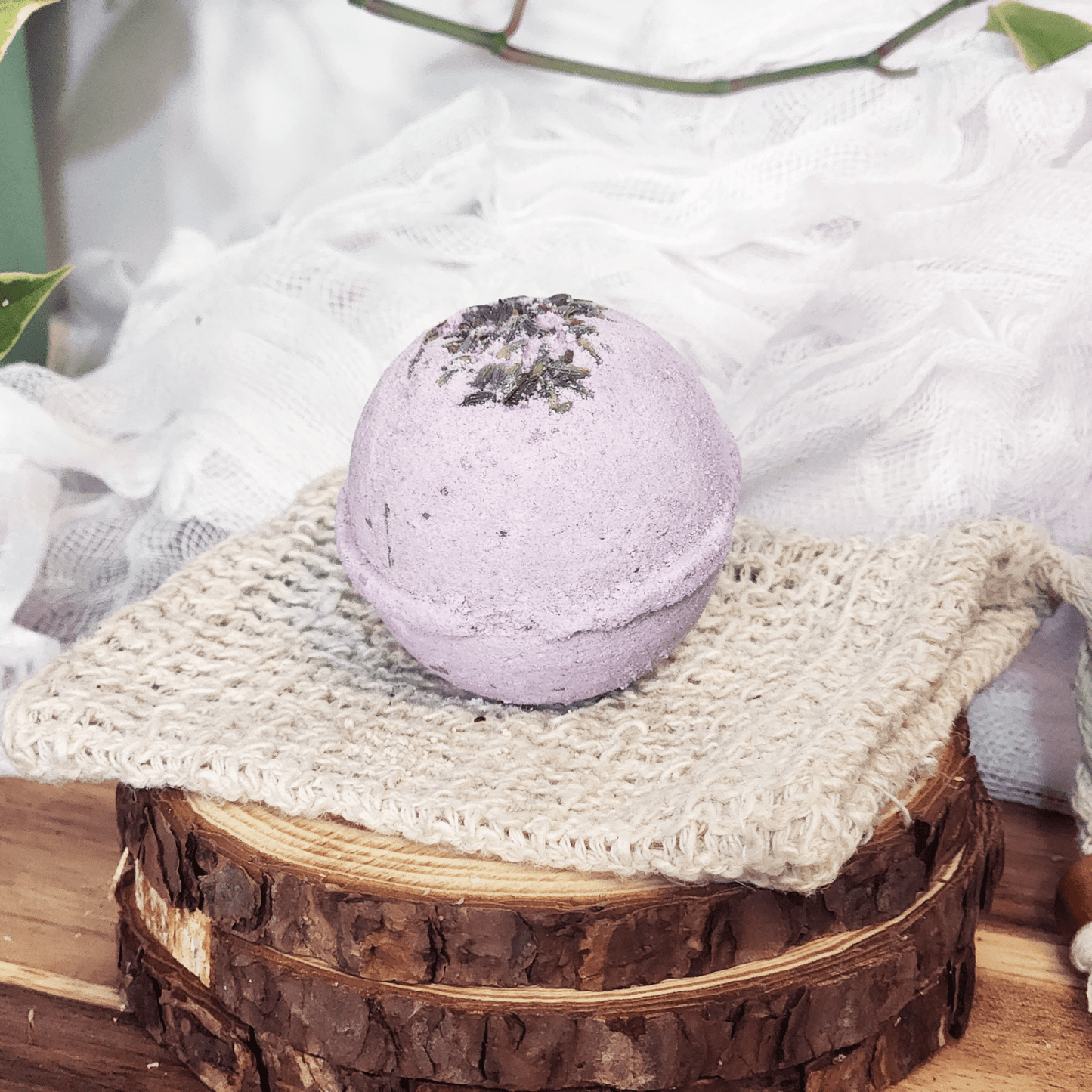 Handmade lavender bath bomb with dried lavender on top displayed on a knitted cloth and wooden rounds