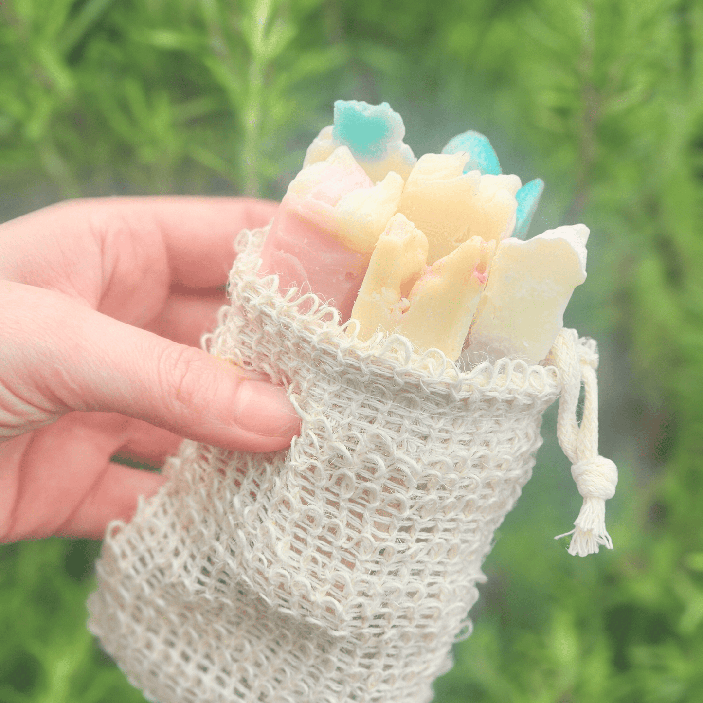 Hand holding a natural soap sampler gift set in a small woven drawstring bag with assorted handmade soaps
