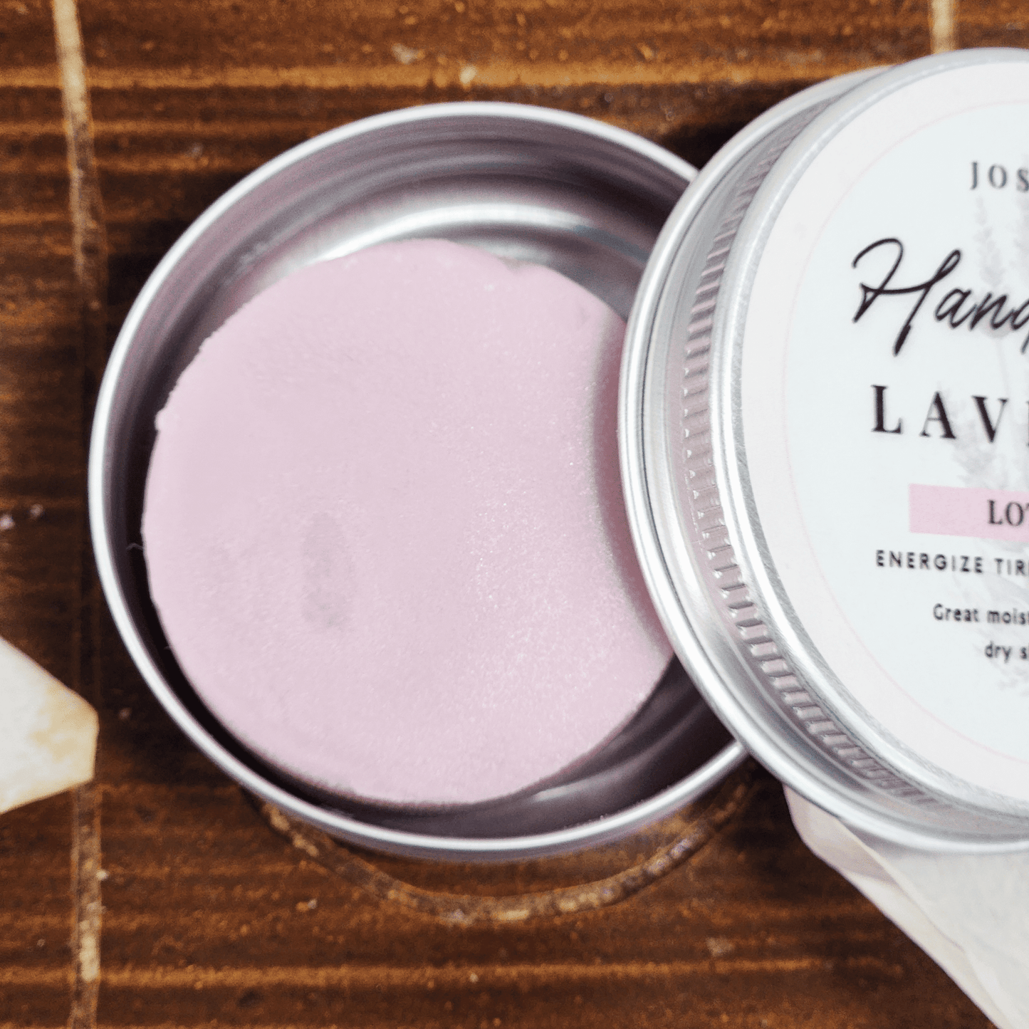 Lavender travel size mini lotion bar in a round metal tin container on wooden surface
