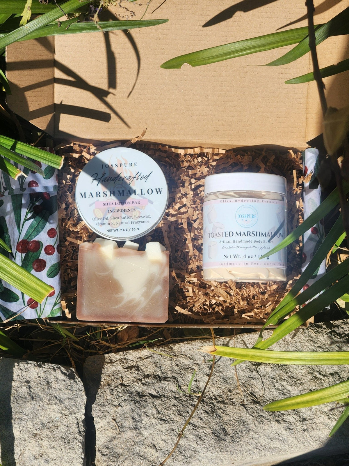 Marshmallow vanilla skincare bundle with soap, cream, and natural ingredients in a kraft box surrounded by shredded paper.