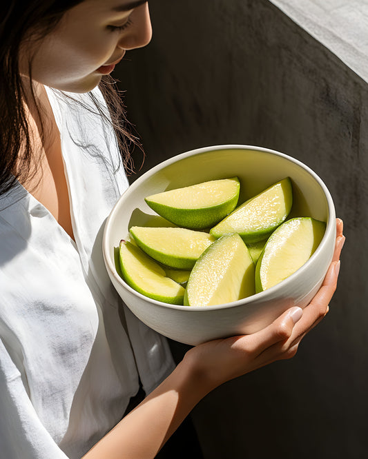 Woman holding bowl of green apple slices representing fresh ingredients for probiotic skincare routine