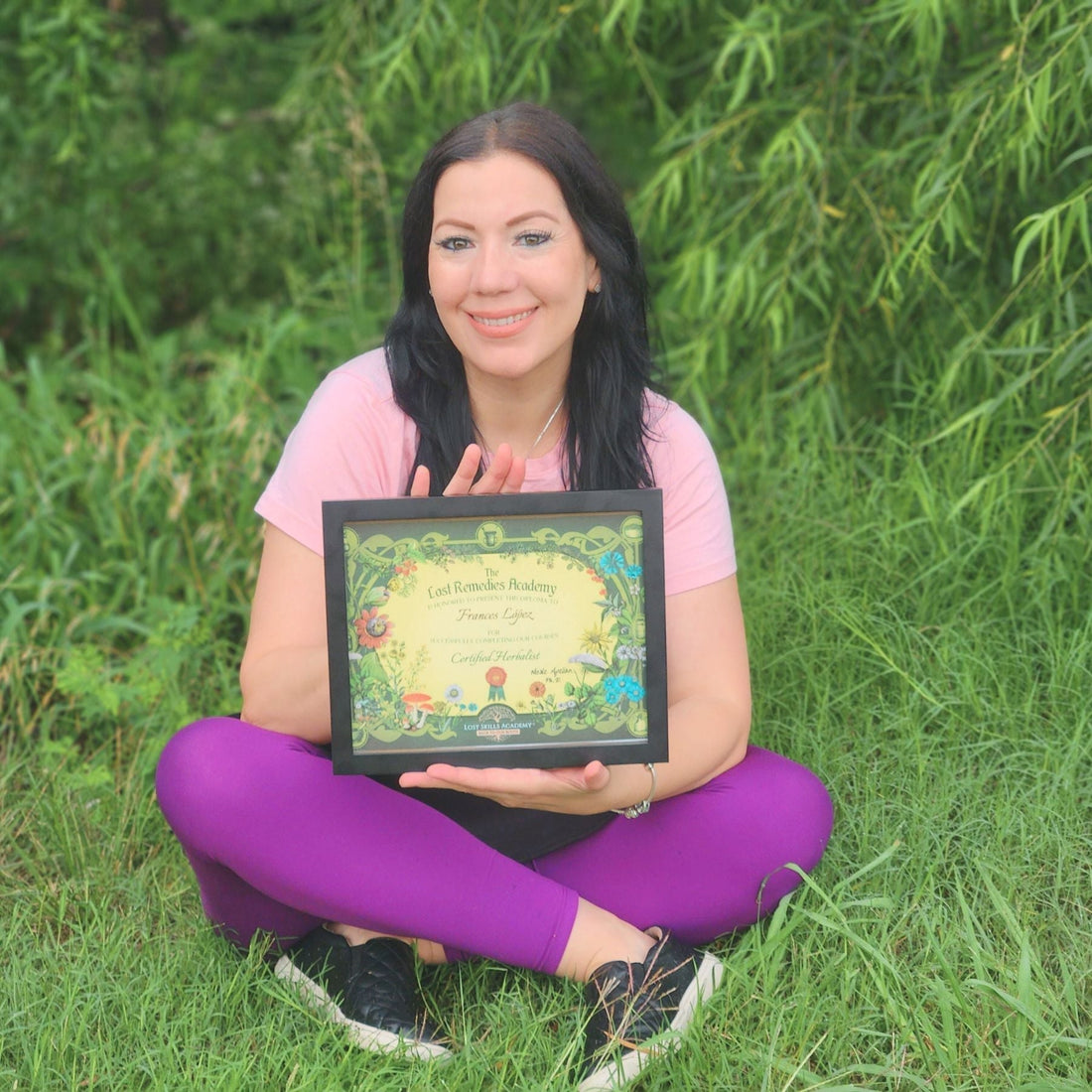 Woman sitting on grass holding a certificate representing herbal wisdom to natural skincare success