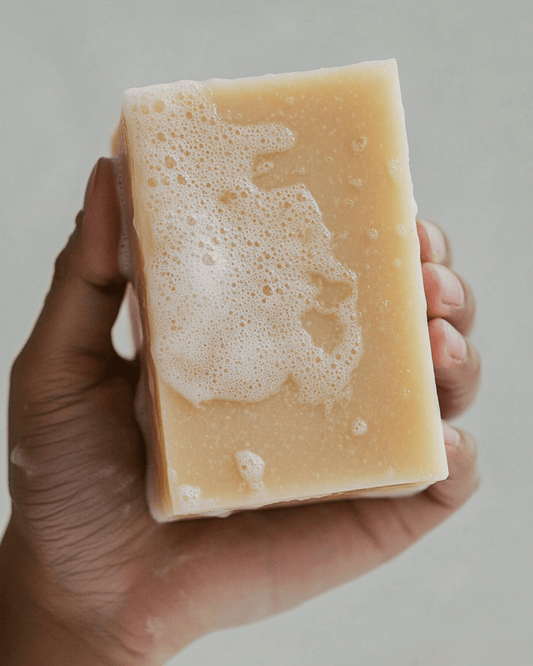 Hand holding a foamy beige bar of artisan soap showing natural texture and gentle cleansing