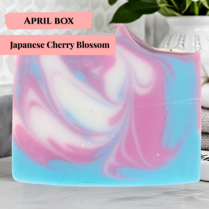 Japanese cherry blossom soap bar with pink and blue swirls, labeled as April box, displayed on a marble surface.