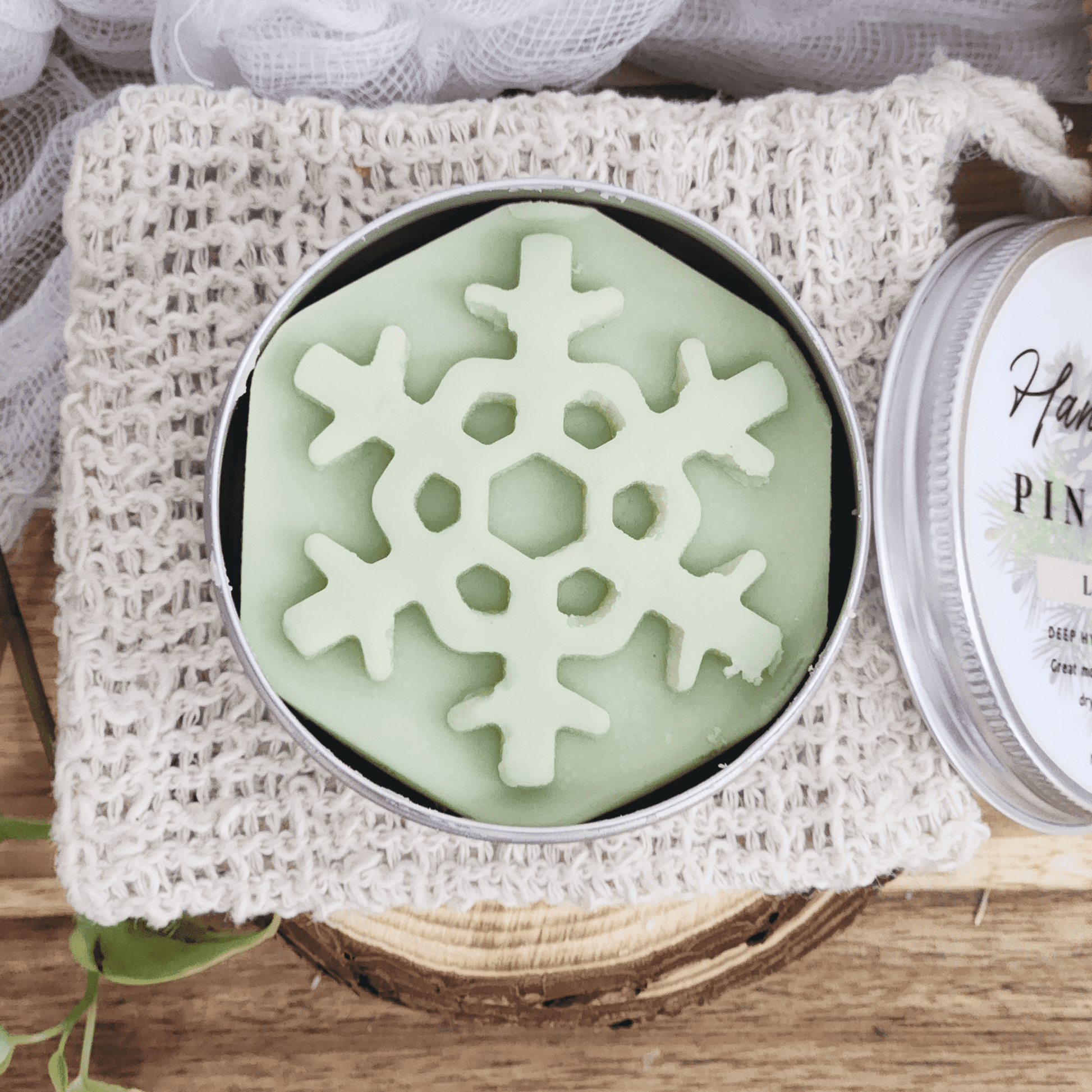 JOSSPURE handmade lotion bars shaped like a green snowflake in a round tin on a knitted pouch