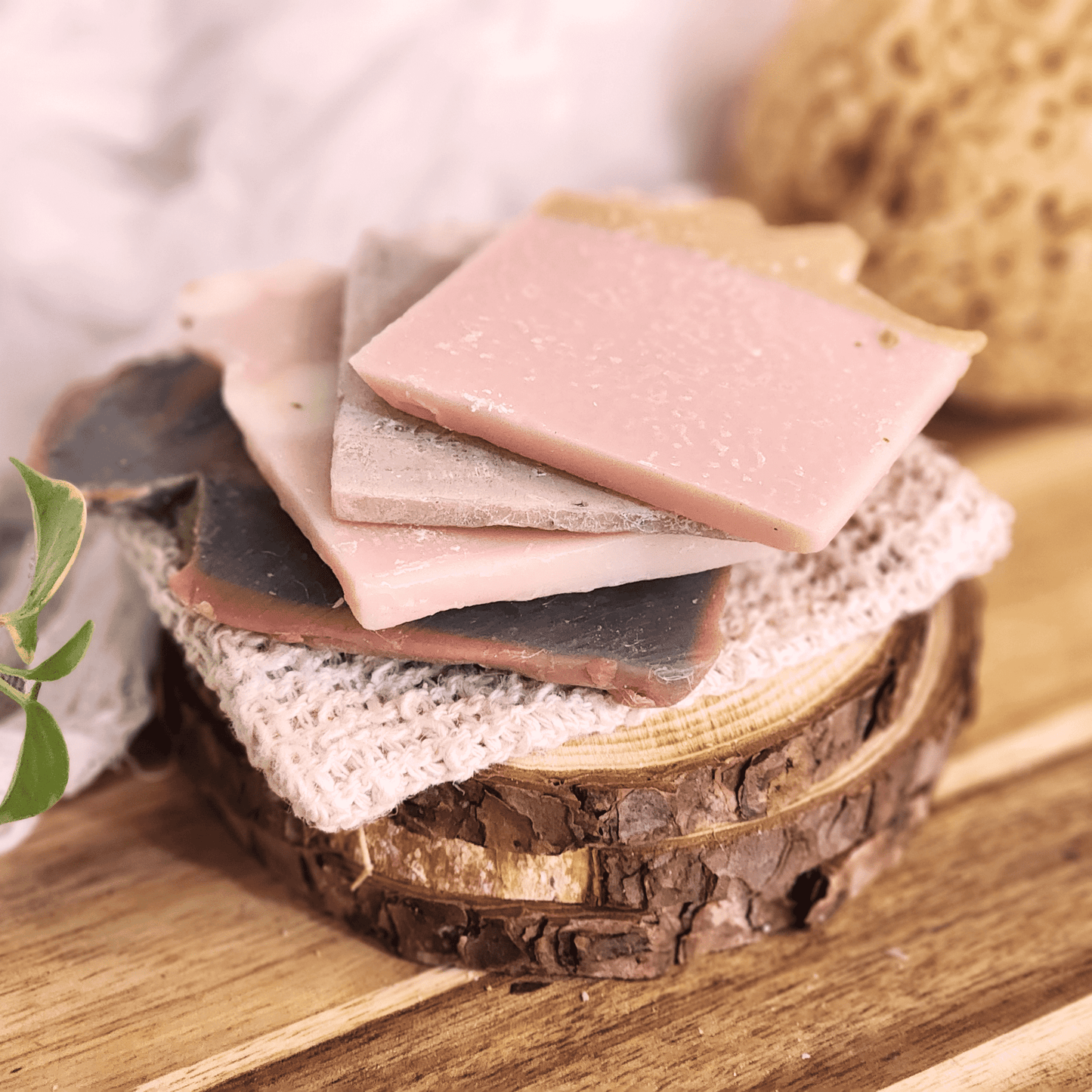 Handmade soap samples and sisal bag displayed on rustic wooden surface with natural textures