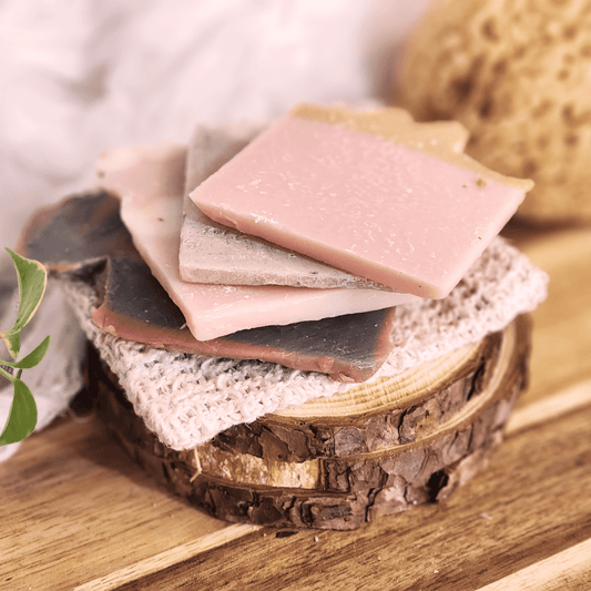 Handmade soap samples and sisal bag displayed on rustic wooden surface with natural textures