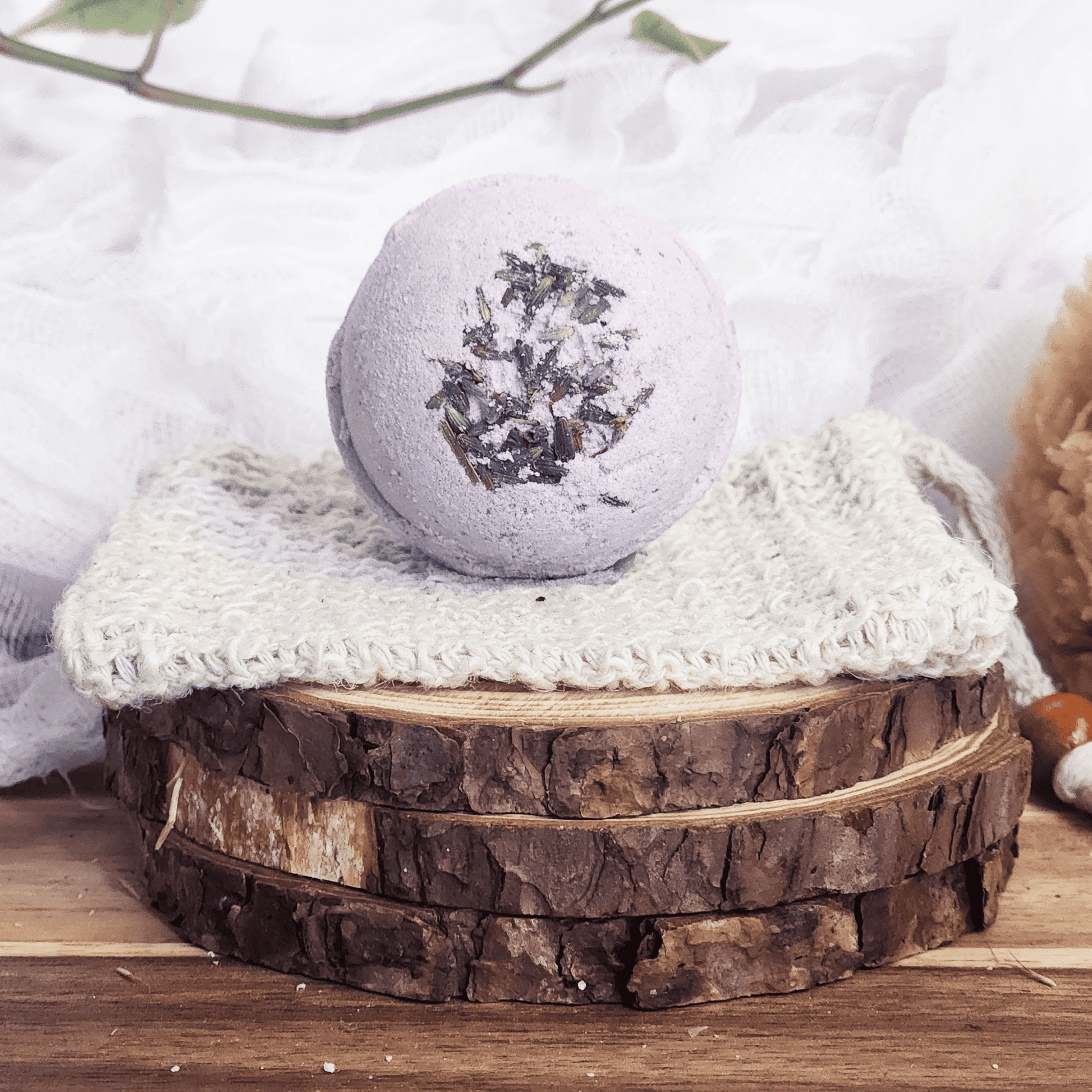 JOSSPURE lavender bath bomb with dried lavender on top placed on a knitted cloth over wooden slices