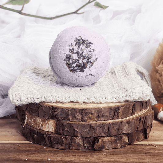 JOSSPURE lavender bath bomb with dried lavender on top placed on a knitted cloth over wooden slices