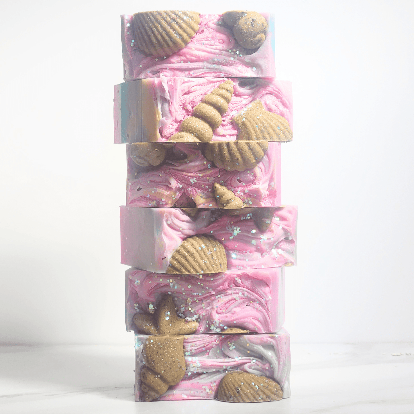 Stack of sea salt shea butter summer soap bars with pink swirls and decorative seashell shapes