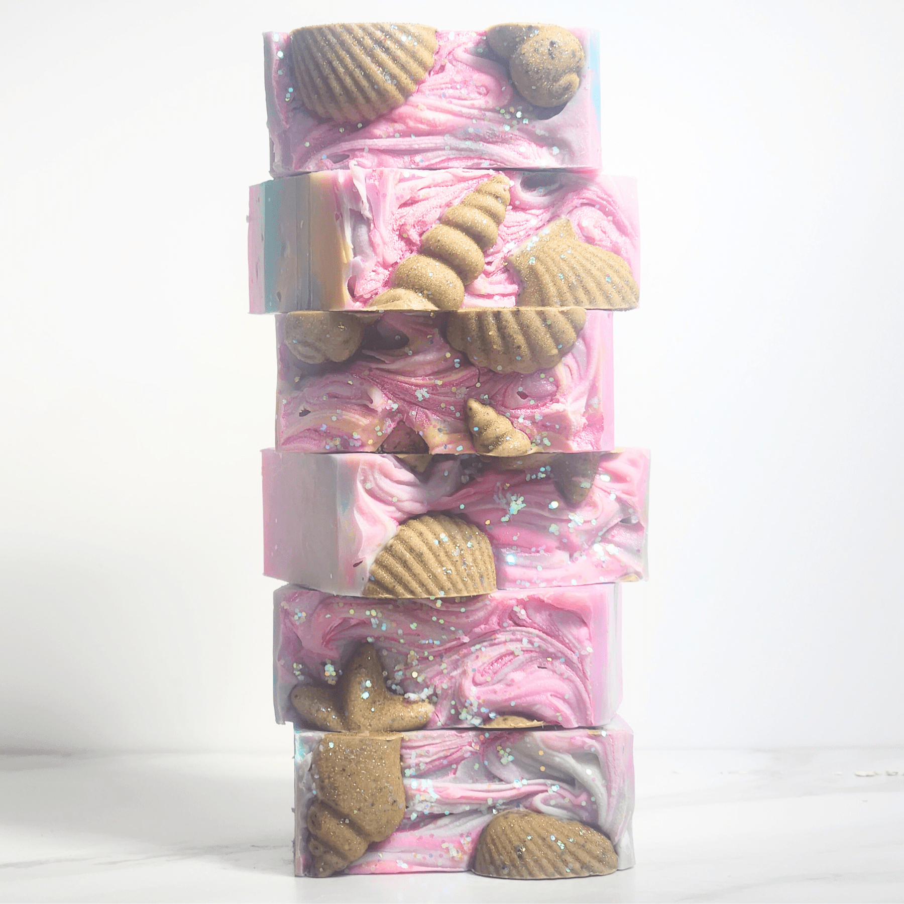 Stack of sea salt shea butter summer soap bars with pink swirls and decorative seashell shapes