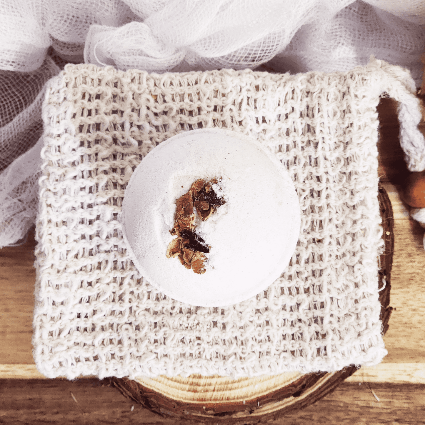 Rose luxury bath bomb with dried flower petals on a woven soap pouch over wooden surface