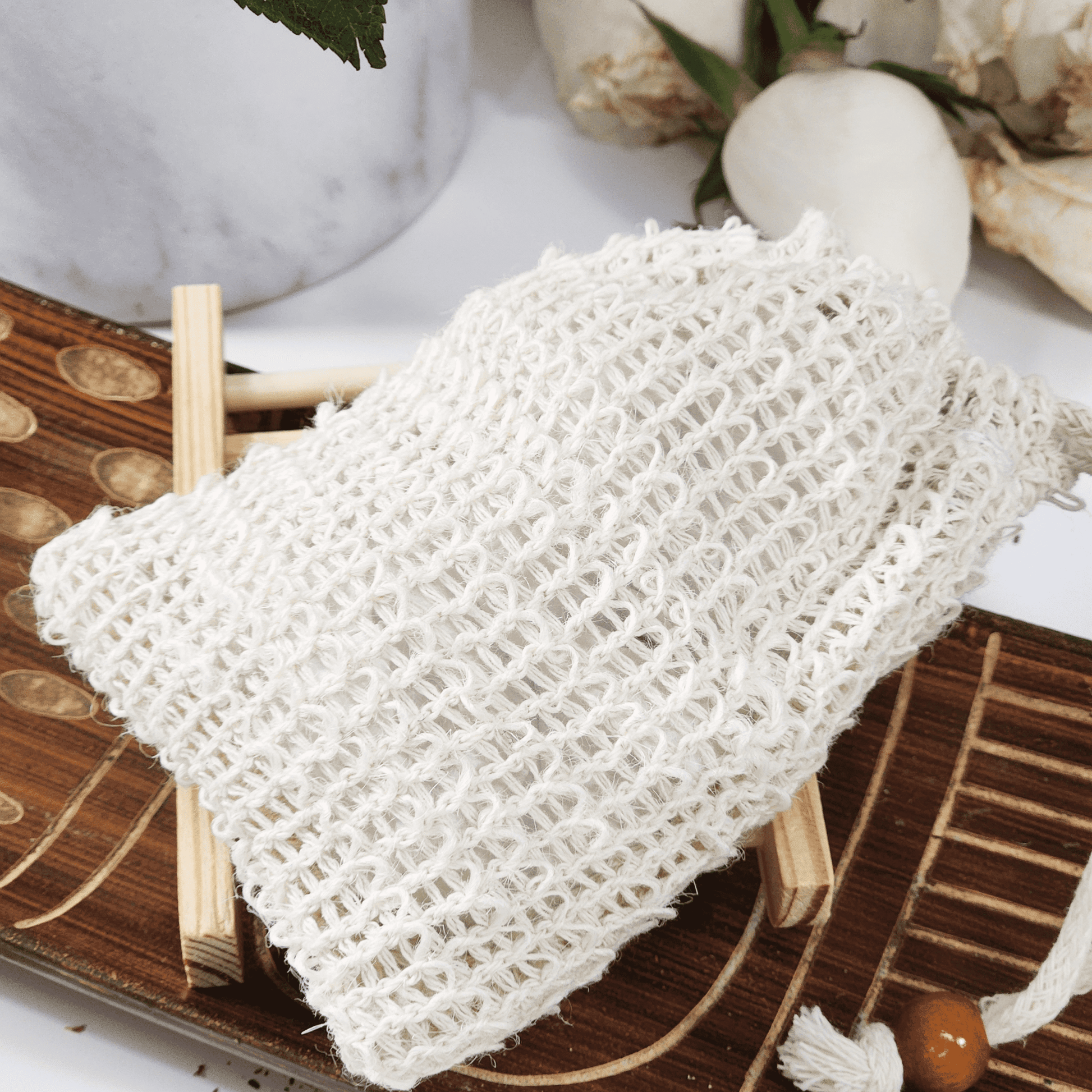 White soap saver and sisal bag for soap displayed on wooden soap dish with natural decor