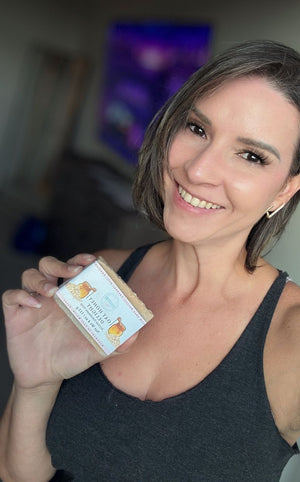 Woman holding a bar of soap with a label, smiling at the camera.