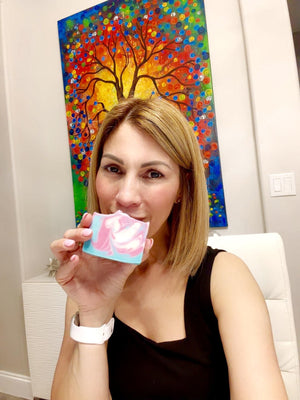 Woman holding a small pink object in front of a colorful abstract painting
